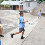 Asian boy kicking football with two boys and girl watching