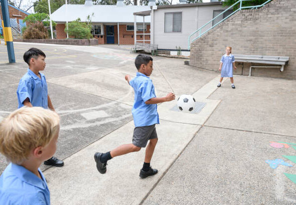 Asian boy kicking football with two boys and girl watching