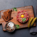 Savory beef tartare with pickled gherkins and brown bread toasts. Flat lay